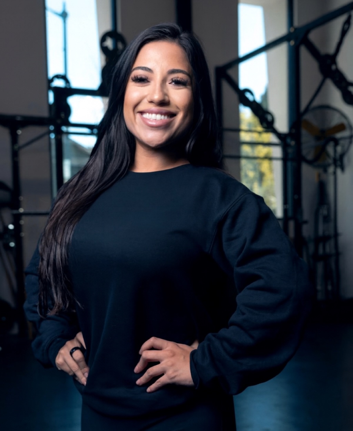 May standing in a gym, smiling, hands on hips.